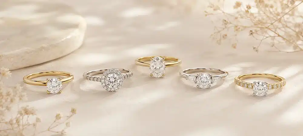 Selección de anillos de compromiso con diamantes en oro amarillo y oro blanco sobre fondo claro.